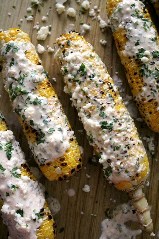 Mexican grilled corn on the cob topped with seasoning and spices on a wooden surface.